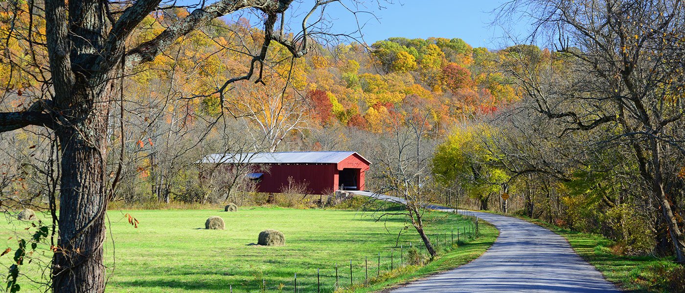 A covered bridge surrounded by autumn foliage and hay bales near Versailles, Indiana — part of the region Clean and Conscious Co. serves.
